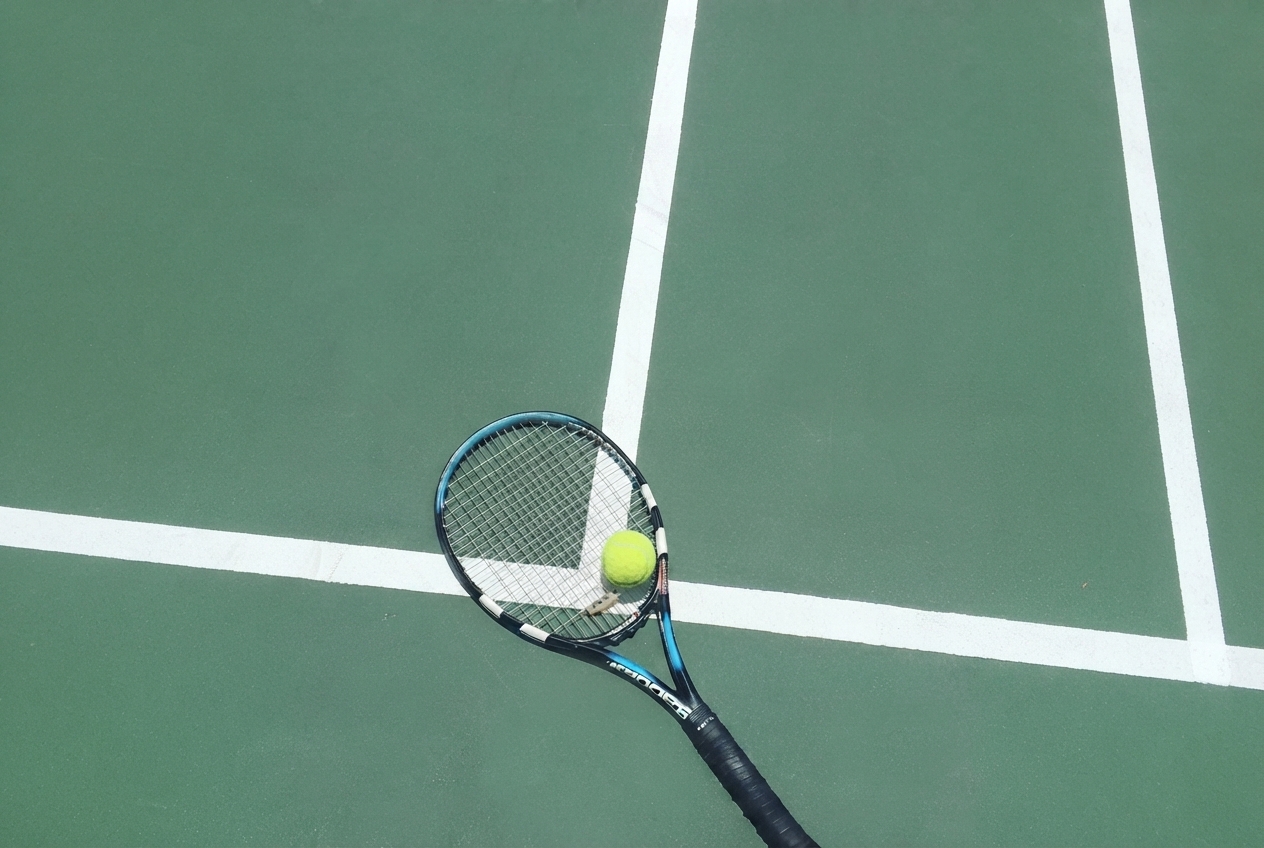 Tennis racket and ball resting on a green court